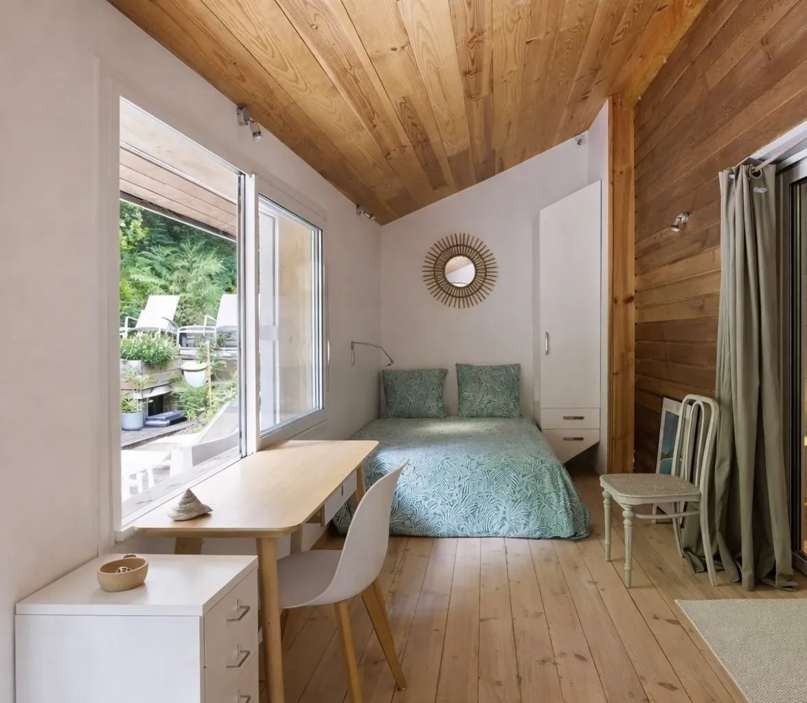 Chambre Océan : lit, bureau et baie vitrée sous un plafond en bois clair