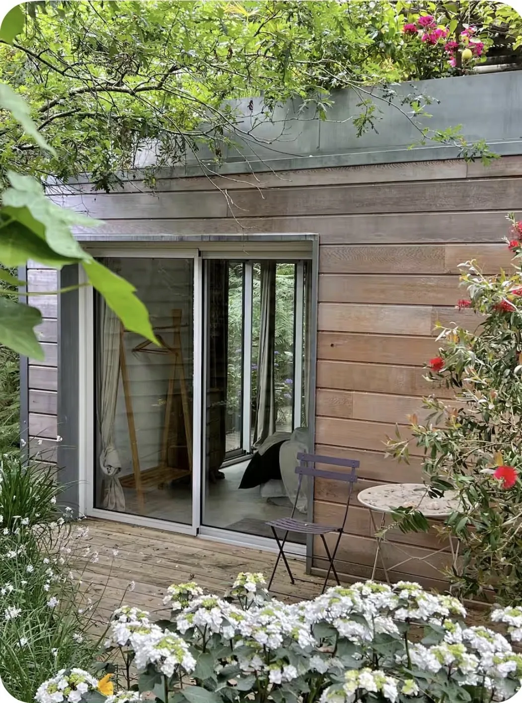 Extérieur de la Chambre des Pins : façade bois, terrasse et petit salon de jardin fleuri