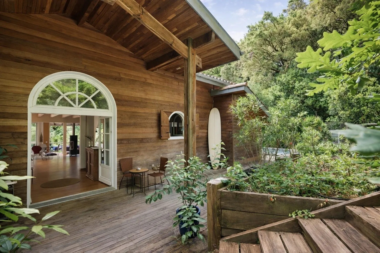 Wooden entrance of Villa Augusta with an arched glass door, a shaded terrace and a view over the greenery